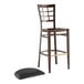 A Lancaster Table & Seating Spartan Series metal bar stool with a black vinyl seat pad and a black footrest.