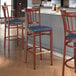 A Lancaster Table & Seating metal slat back bar stool with mahogany wood grain finish and navy vinyl seat.