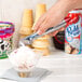 A person using a Vollrath red aluminum ice cream scoop to scoop ice cream into a bowl.