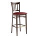 A Lancaster Table & Seating metal slat back bar stool with dark walnut wood grain finish and burgundy vinyl seat.