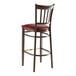 A Lancaster Table & Seating metal slat back bar stool with dark walnut wood grain finish and a burgundy vinyl seat.