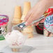 A hand holding a Vollrath aluminum ice cream scoop over a bowl of ice cream.