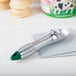 A silver metal Vollrath ice cream scoop with a green handle on a white surface.