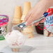 A hand using a Vollrath blue aluminum ice cream scoop to scoop ice cream into a bowl.