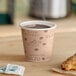A Choice tall cafe print paper hot cup filled with coffee on a counter next to a pastry.