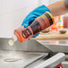 A person in blue gloves pouring 3M Liquid Griddle Quick Clean onto a grill.