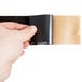 A hand holding a black piece of paper with a brown and black strip of 3M Safety-Walk tape.