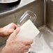 A hand holding a 3M Scotch-Brite light-duty scrub sponge over a glass.