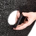 A hand holding a black 3M High Productivity Stripping Floor Pad.