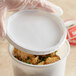A hand holding a Choice white plastic deli container filled with food.