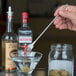 A hand holding an American Metalcraft stainless steel bar fork over a martini glass.