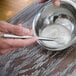 A person using an American Metalcraft stainless steel mini bar whisk to mix food in a bowl.