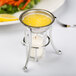 A Vollrath butter melter cup with a lit candle on a table with yellow liquid inside.