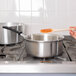 A person stirring sauce in a Vollrath stainless steel sauce pan on a stove.