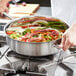 A person using a Vollrath Intrigue saute pan to cook food on a counter.