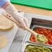 A person in gloves using a Carlisle long handle portion spoon to serve guacamole.