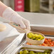 A person in gloves using a Carlisle beige and green color coded perforated portion spoon to serve sliced jalapenos.