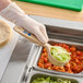 A person holding a Carlisle Measure Misers short handle solid portion spoon with lettuce in a container.