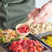 A person using a Carlisle beige and red color coded perforated portion spoon to serve food.