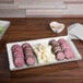 An American Metalcraft antique white melamine platter with sliced meats and cheese on a table.