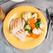 A plate of food with chicken and vegetables on a GET Diamond Mardi Gras Tropical Yellow melamine plate.