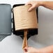 A hand holding a roll of brown natural kraft center pull paper towels.