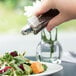 A hand pouring salt from a Tablecraft Metro glass shaker onto a salad.