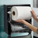 A large white hardwound paper towel roll being placed into a black wall-mounted dispenser.