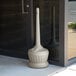 A round beige Commercial Zone Smokers' Outpost cigarette receptacle with a round cap on the ground.