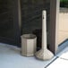 A beige Commercial Zone Smokers' Outpost cigarette receptacle with a black snap-lock lid attached to a white post.