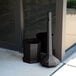 A black Commercial Zone Smokers' Outpost receptacle next to a glass door.