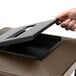 A hand putting a brown lid with an ashtray onto a brown square waste container.