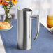 An American Metalcraft satin finish stainless steel pitcher on a table with flowers.