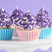 A group of cupcakes with white frosting and purple sprinkles in pink and blue wrappers on a white cake stand.