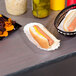 A white plastic table cover on a table with a hot dog in a bun and a basket of chips.