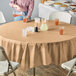 A table with a Creative Converting Glittering Gold OctyRound table cover and glasses of orange liquid.