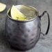 A Libbey hammered antique copper Moscow mule mug filled with a lime wedge in it.