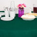 A table with a Hunter Green OctyRound table cover, plates, and utensils on it.