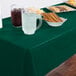 A table with food and drinks covered by a Creative Converting Hunter Green plastic table cover.