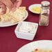 A person dipping a piece of bread into a white square bowl with dip.