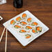 A Libbey Slate porcelain plate with sushi on a table.