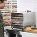 A man putting orange slices on a tray in an Avantco stainless steel food dehydrator.