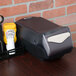 A black San Jamar countertop napkin dispenser on a table.