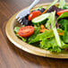 A Creative Converting Glittering Gold paper plate with salad and a fork on it.