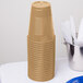 A stack of Creative Converting glittering gold plastic cups on a table.