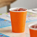 A Sunkissed orange paper cup with ice and fruit on a table.