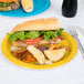 A sandwich and potato chips on a school bus yellow paper plate.