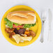 A School Bus Yellow paper plate with a sandwich and potato chips on it.