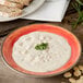 A Carlisle Fireball melamine rimmed soup bowl filled with soup and topped with chives on a table.