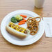 A Dart Concorde white foam plate with a hot dog, pretzels, and a drink on it.